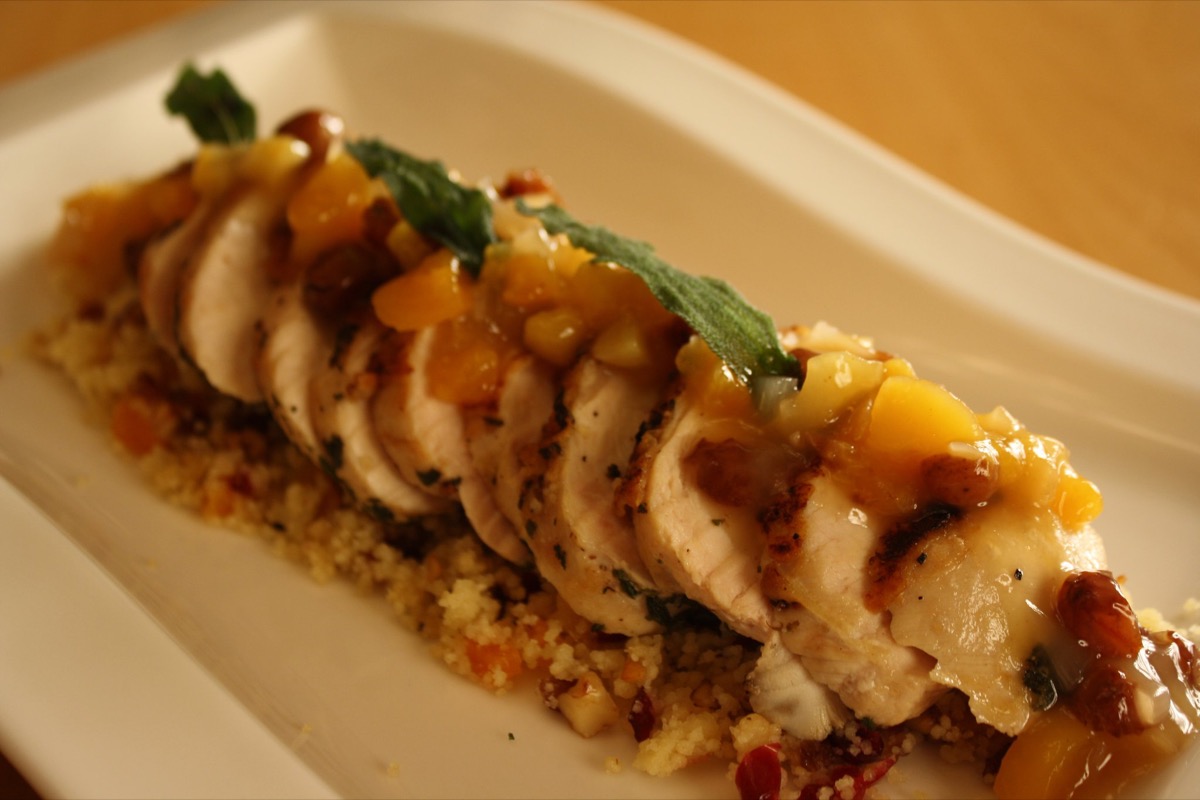 Sliced herb chicken roulade with mango sauce on couscous