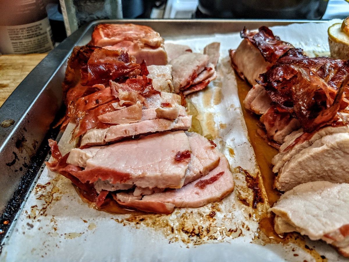 Sliced prosciutto-wrapped pork loin on a baking sheet