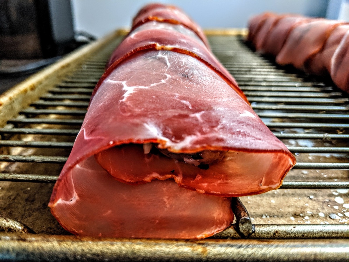 Prosciutto-wrapped pork tenderloin roulades on a rack before roasting
